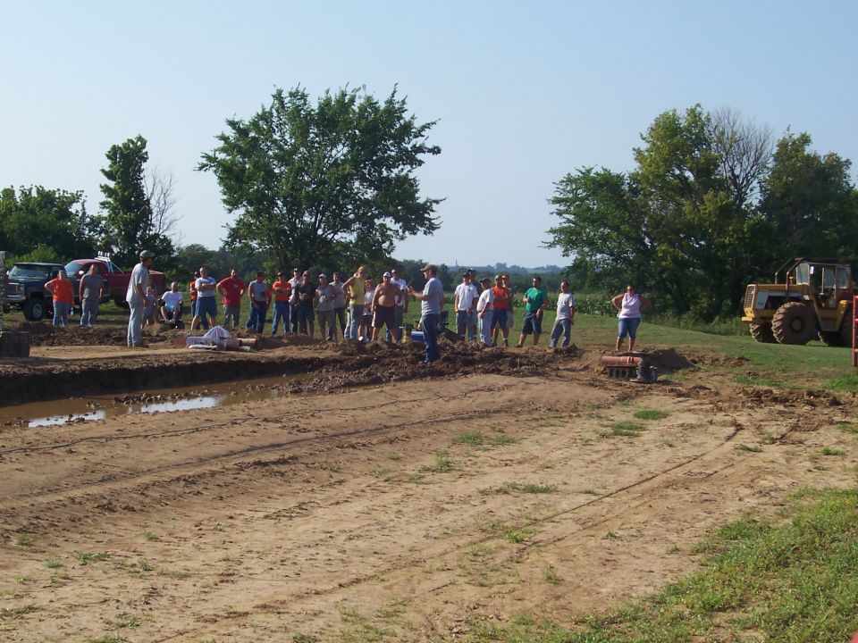 Group of people and trucks near a muddy track with a yellow tractor.