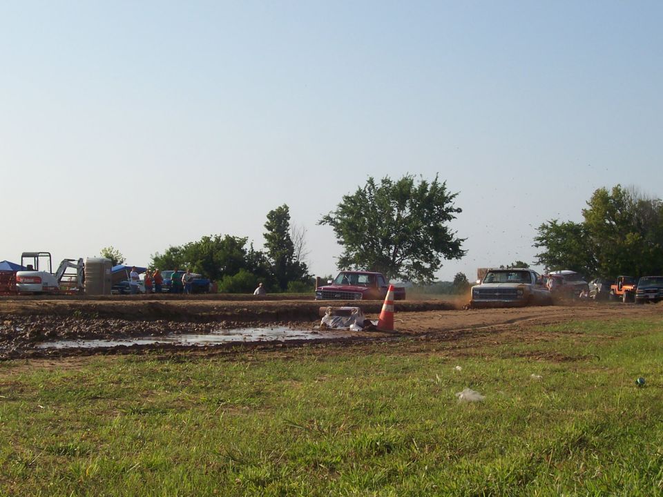 White pickup truck stuck in mud pit at an outdoor event.