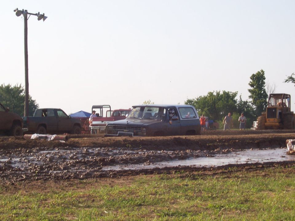 Blue SUV stuck in mud with a bulldozer in the background at a mud bogging event.