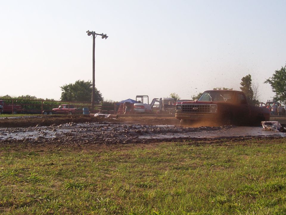Red pickup truck driving through a mud pit, splashing mud.