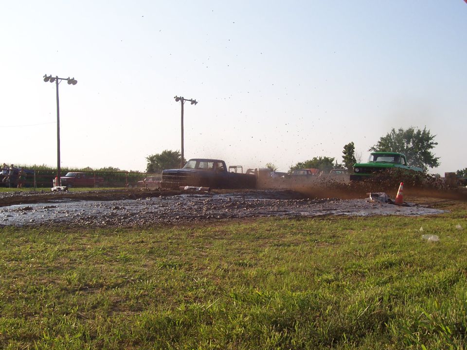 Mud bogging competition with two pickup trucks spraying mud.
