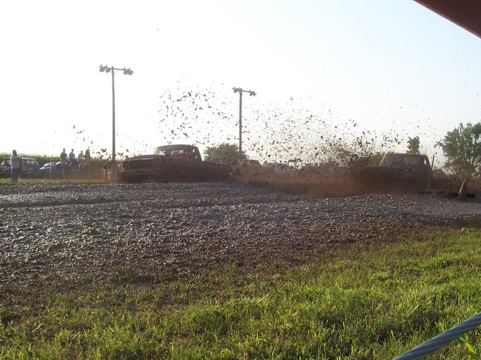 Two pickup trucks in a mud bog, spraying mud high into the air.