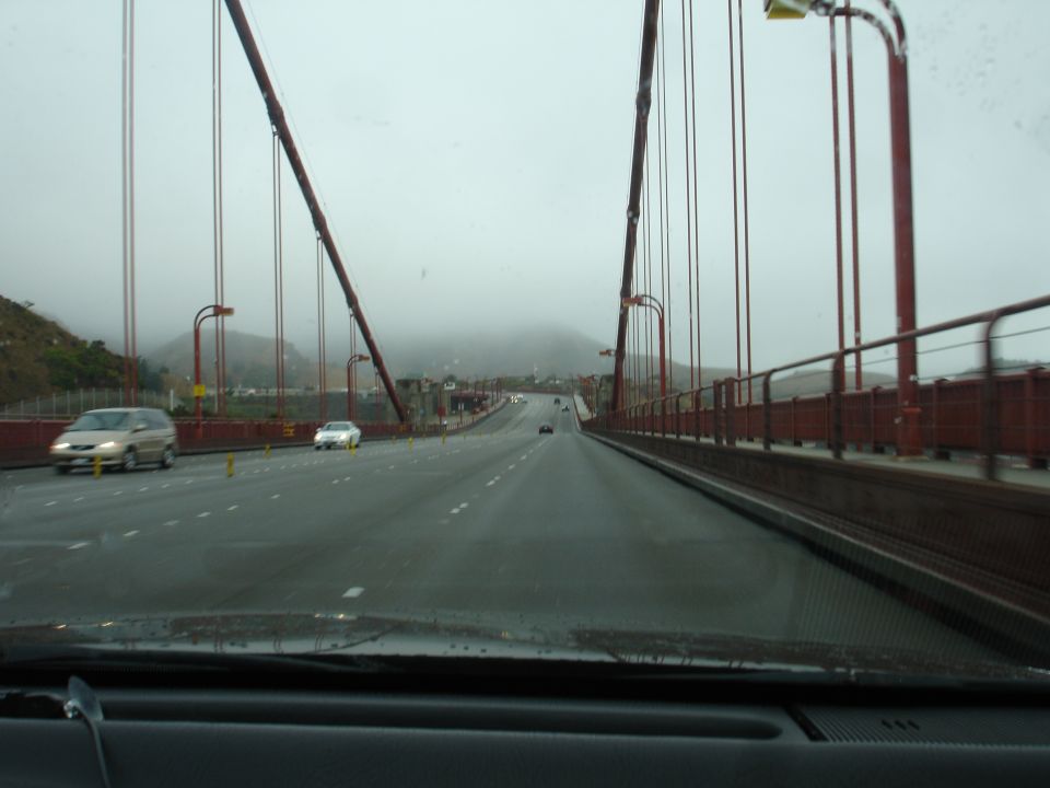 Tan minivan on a bridge with fog in the background, viewed from inside another car.