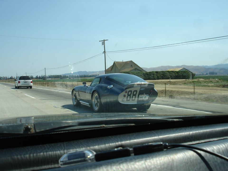 Blue Shelby Cobra Daytona Coupe replica with white stripes and '88' on the rear driving on a highway, white SUV in distance
