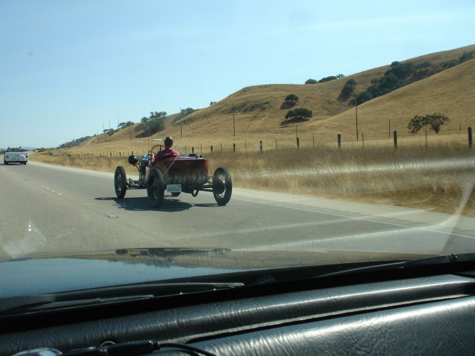 Hot rod with a red driver's seat and wooden body, seen from behind on a highway