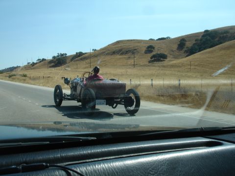 1990 Ford Taurus - A vintage red roadster is seen from another vehicle on a highway, with a driver wearing a red shirt and a hat.