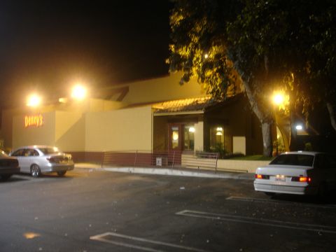 1990 Ford Taurus - Two cars are parked in a lot outside a Denny's restaurant at night.