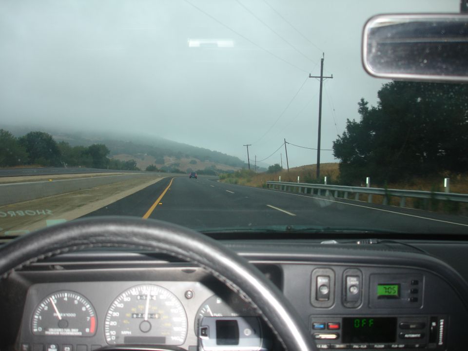 Interior view of a 1990 Ford Taurus dashboard and steering wheel on a highway