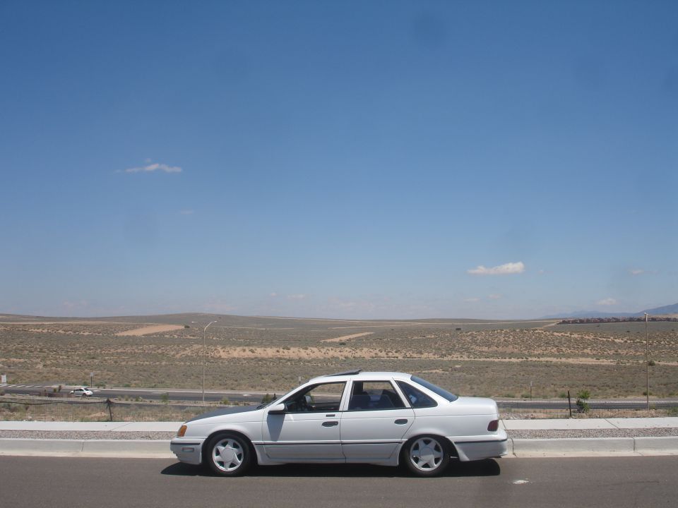 White lowered sedan parked in profile on desert roadside under blue sky