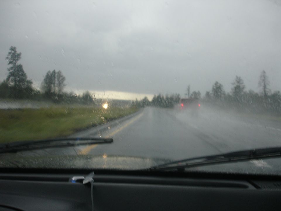 Driver's view through a rainy windshield of a wet highway with a red vehicle ahead