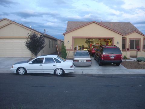 1990 Ford Taurus - Three vehicles are parked in front of a house, one is a 1990 Ford Taurus.