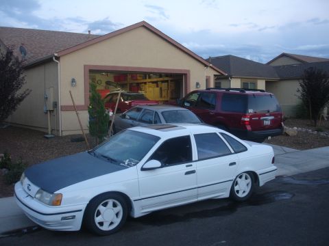 1990 Ford Taurus - A white sedan with a dark hood is parked in front of a suburban garage, with other vehicles present.