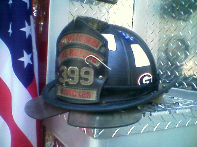 Black leather fire helmet marked 399 and K. Stokes on diamond plate beside a US flag