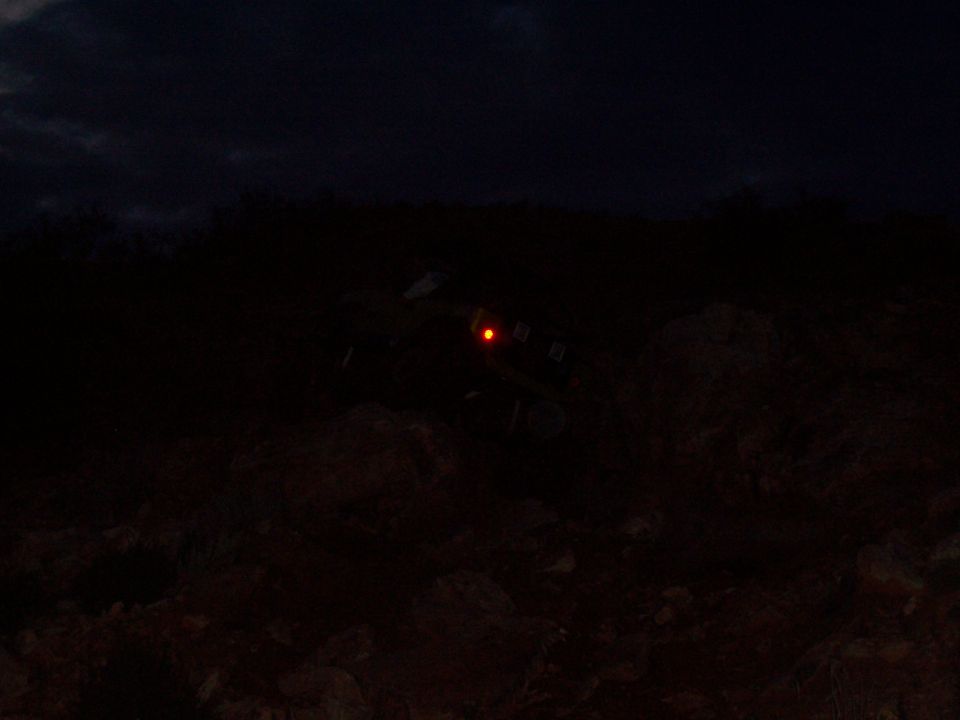 Dark nighttime scene of an off-road vehicle with a red light among rocks