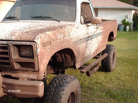 1982 Ford F-100 - A heavily mud-covered 1980s Ford F-100 pickup truck is parked on a grassy lawn in front of a house. The truck has large off-road tires and…