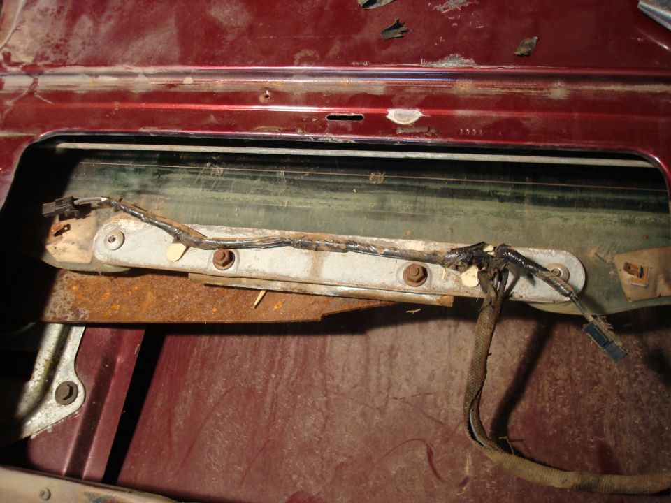 Power window regulator and motor exposed inside a dark red tailgate with trim removed