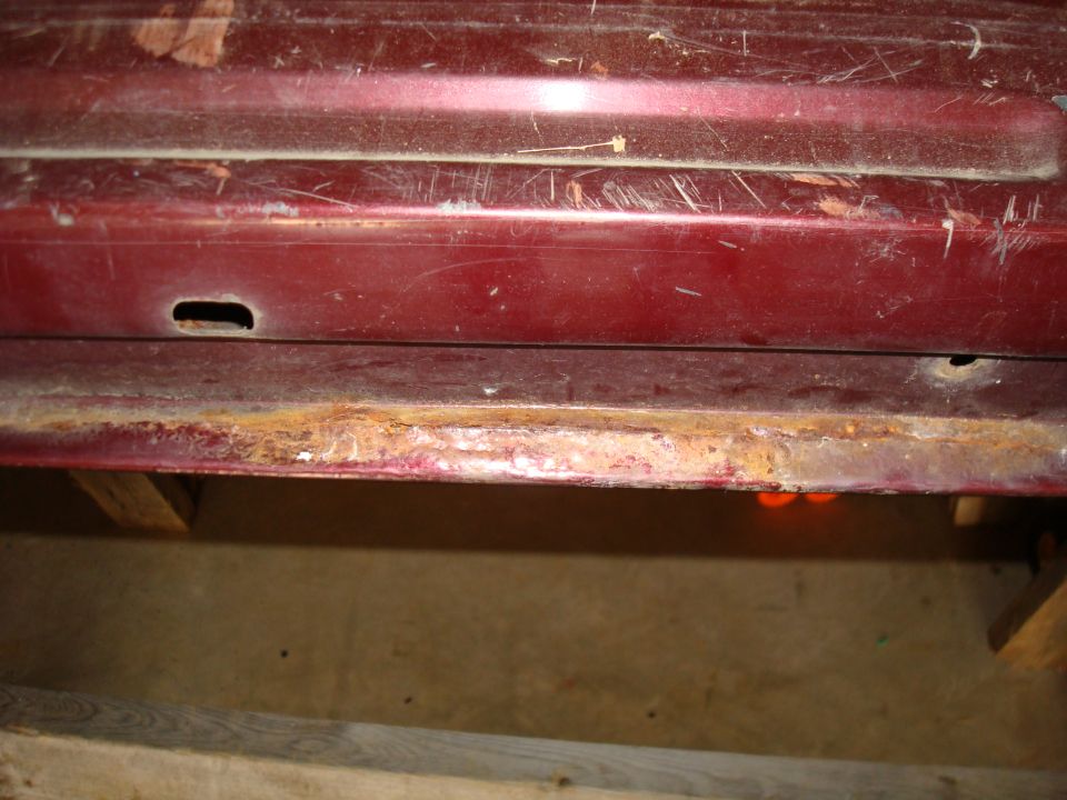 Close-up of rusted lower panel on a dark red vehicle.