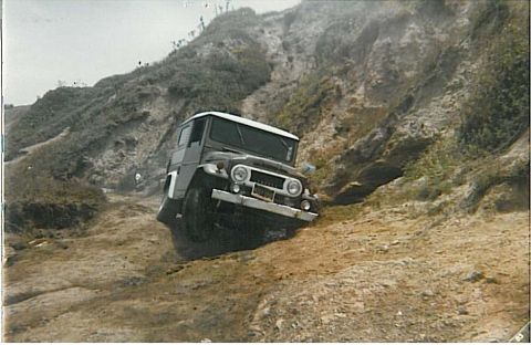 1991 Ford Bronco - Vintage film photo of a dark Toyota Land Cruiser FJ40-style hardtop 4x4 with a white roof tipped at an angle on an eroded dirt hillside tra…