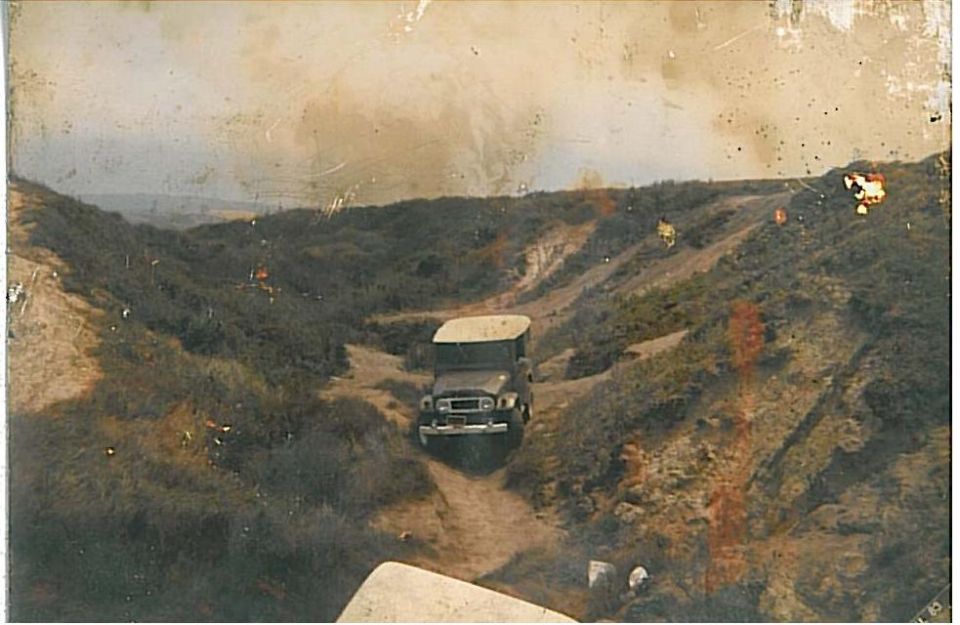 Dark soft-top SUV driving on a dirt path through hilly terrain.