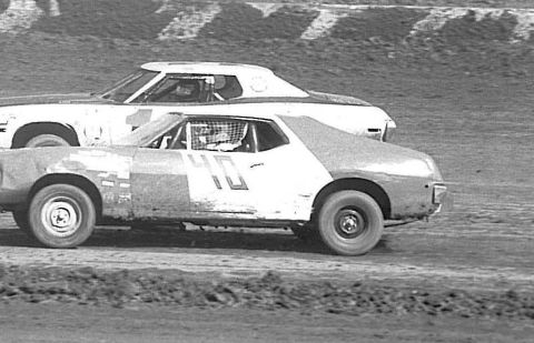 1991 Ford Bronco - Two stock cars race on a dirt track. The car in the foreground is white with red and blue accents and the number 40 visible on its side.