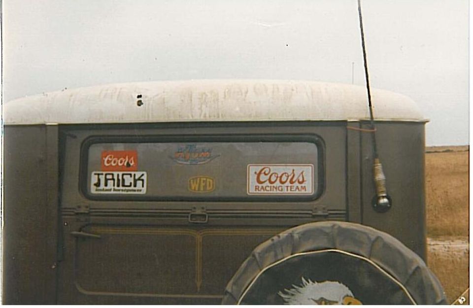 Rear window of olive vintage wagon with Coors Racing Team decals and eagle spare tire cover