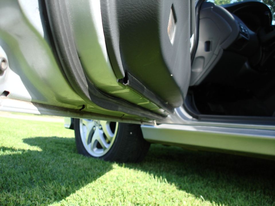 Low-angle shot of an open car door showing rocker panel, gray door trim and alloy wheel