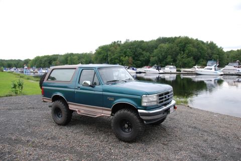1996 Ford Bronco - Photograph of a green Ford Bronco parked on gravel beside a marina full of boats.