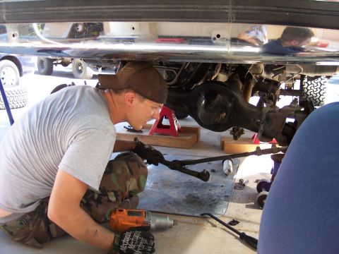 1996 Ford Bronco - A mechanic works on the undercarriage of a vehicle, focusing on the suspension and steering components. An orange impact wrench and various…