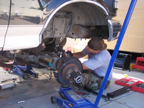 1996 Ford Bronco - A person works on the suspension of a dark blue and white Ford Bronco, which is supported by hydraulic jacks. Tools and car parts are scatt…
