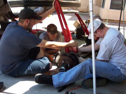 1996 Ford Bronco - Three men are working on the suspension of a vehicle, which is elevated by red jack stands. One man is holding a red metal bar, while the o…