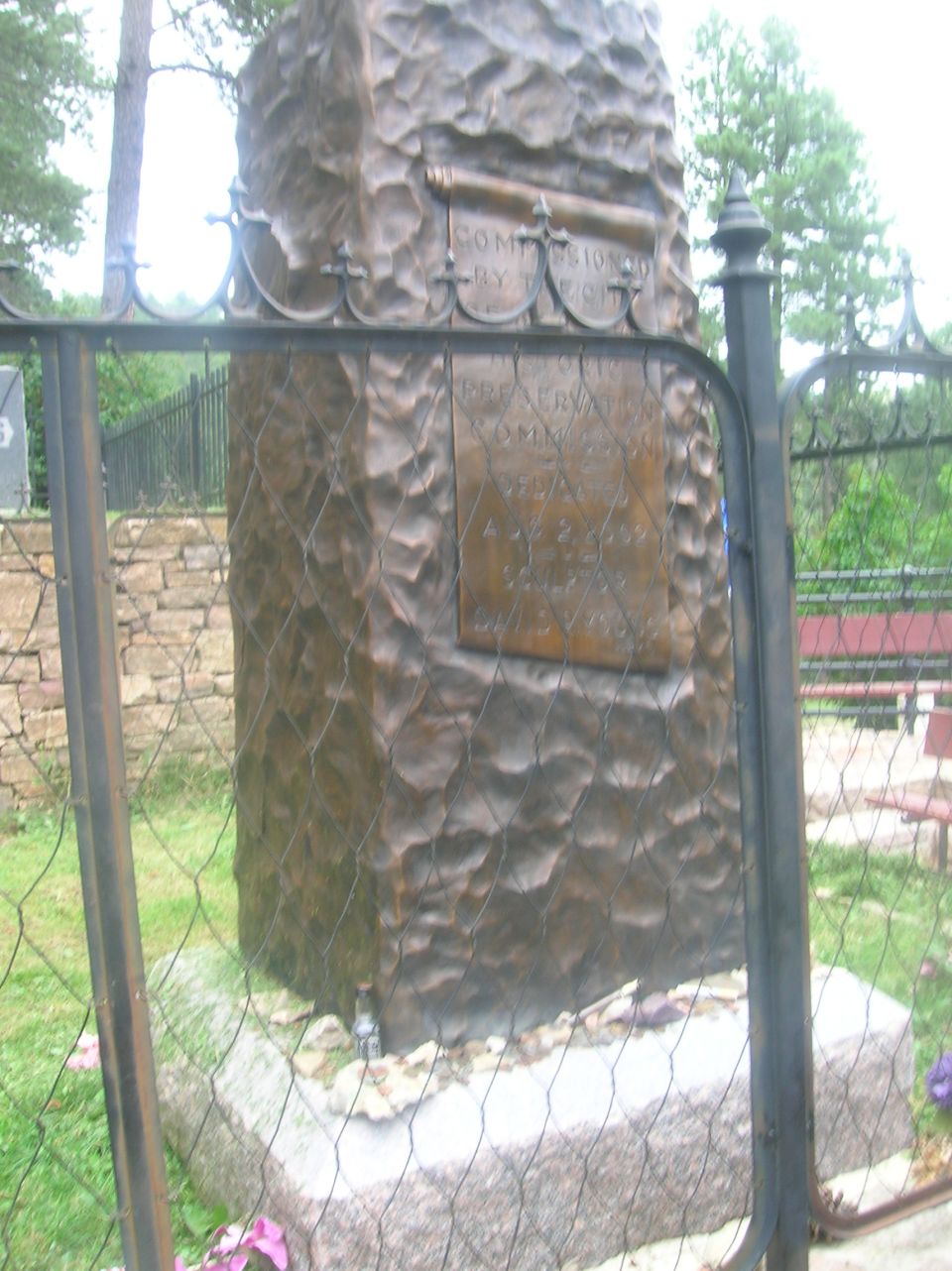 Stone pillar behind a black metal fence with greenery in the background