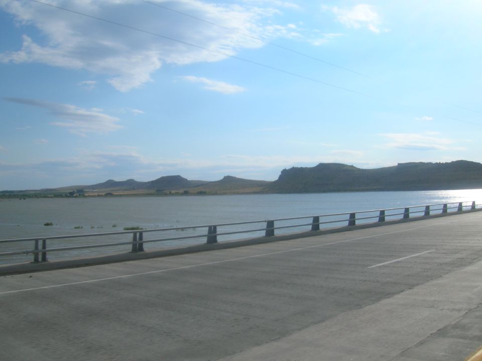 View from a bridge crossing a wide lake with hills in the distance under a partly cloudy sky