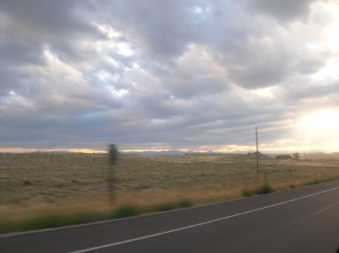 1996 Ford Bronco - A view from a moving vehicle captures a vast, grassy landscape under a dramatic, cloudy sky as the sun sets on the horizon.