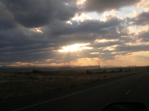 1996 Ford Bronco - Sunbeams pierce through dramatic clouds, illuminating a vast landscape and a lonely highway stretching into the distance.