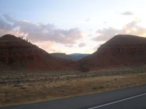 1996 Ford Bronco - A scenic view of red rock formations and rolling hills under a pastel sky, captured from a moving vehicle.