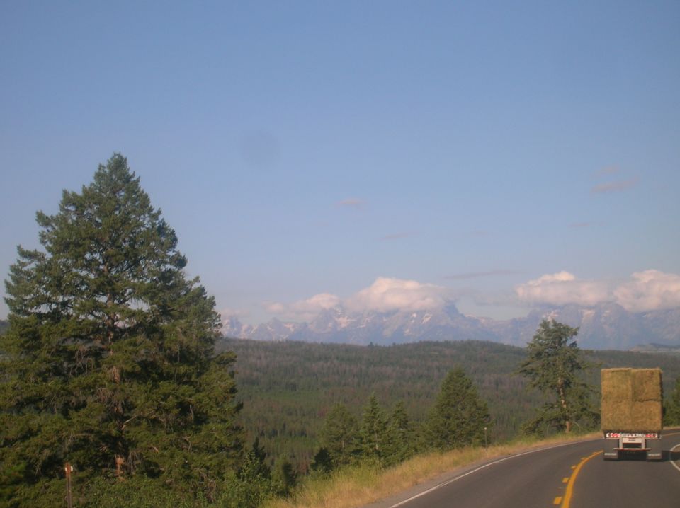 Truck with hay bale on highway, mountains in background