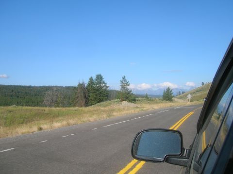 1996 Ford Bronco - View from the passenger side of a vehicle driving on a two-lane road through a scenic landscape with mountains in the distance. The side mi…