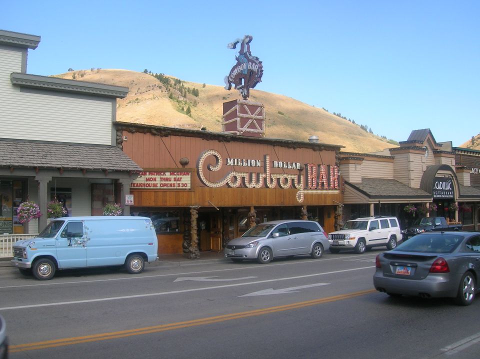 Street view of Million Dollar Cowboy Bar with a blue van, silver minivan, white SUV, and gray sedan parked