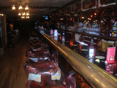 1996 Ford Bronco - The interior of a bar features saddle-shaped seats and a long brass rail along the counter.