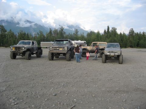 1990 Ford F-250 - Several modified trucks and an SUV are parked on a gravel lot with a mountainous backdrop.