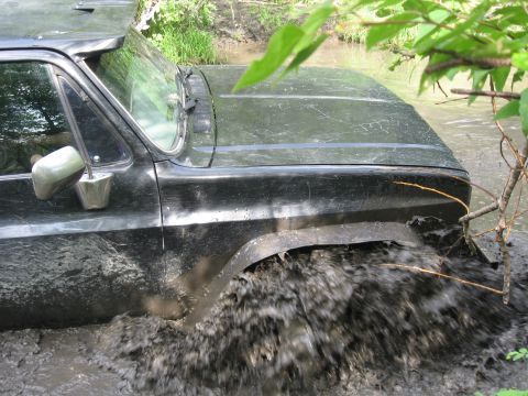 1990 Ford F-250 - Black pickup truck is stuck in mud and water, splashing heavily.