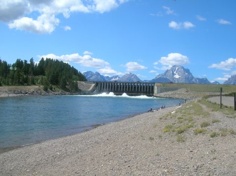1996 Ford Bronco - A scenic view of a dam with water cascading down, set against a backdrop of mountains under a partly cloudy sky.
