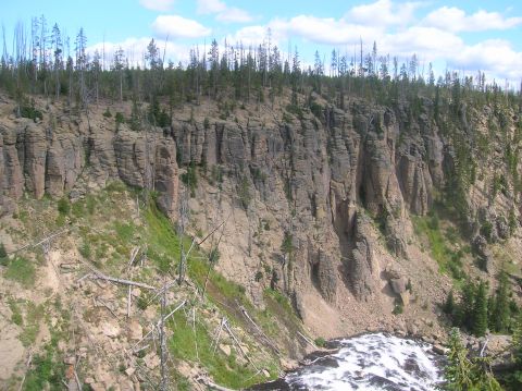 1996 Ford Bronco - A view of a rocky cliff face overlooking a river, with trees on top and scattered on the slope.