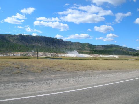 1996 Ford Bronco - View of a geothermal area with steam vents and distant mountains, seen from a roadside perspective.