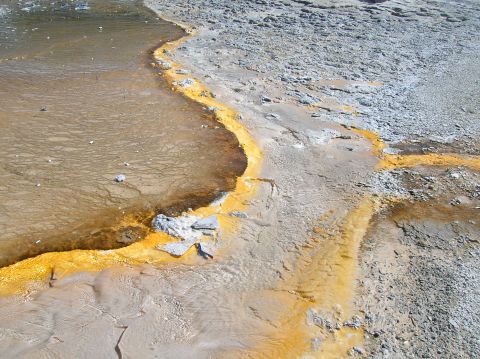 1996 Ford Bronco - A geothermal pool displays vibrant orange mineral deposits against a backdrop of textured, dry earth.