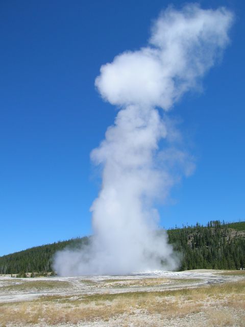 1996 Ford Bronco - A geyser erupts, sending a massive cloud of steam high into the clear blue sky above a treeline and dry, grassy terrain.