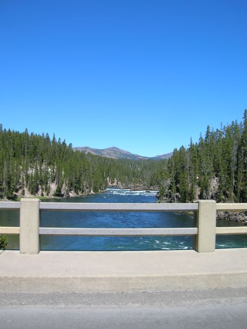 1996 Ford Bronco - A wide river flows through a forested canyon under a clear blue sky. A concrete bridge railing is in the foreground.