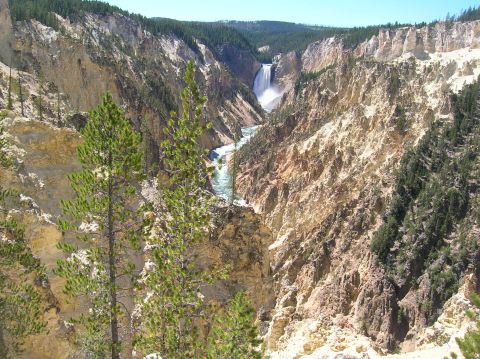 1996 Ford Bronco - A wide view of a deep canyon with a waterfall cascading into a river at the bottom. The canyon walls are steep and rocky, with pine trees g…