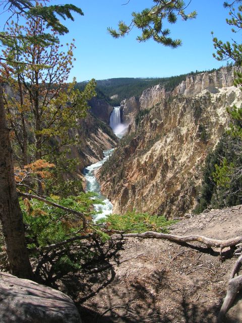 1996 Ford Bronco - A wide view of a canyon with a waterfall cascading into a river below. The scene is framed by trees and rocky cliffs under a clear blue sky.