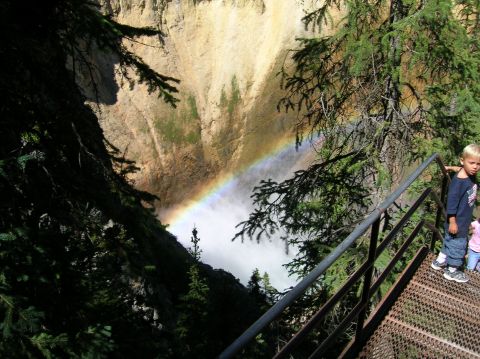 1996 Ford Bronco - A young boy stands on a metal walkway overlooking a canyon with a waterfall and a rainbow. Dense evergreen trees frame the scene.